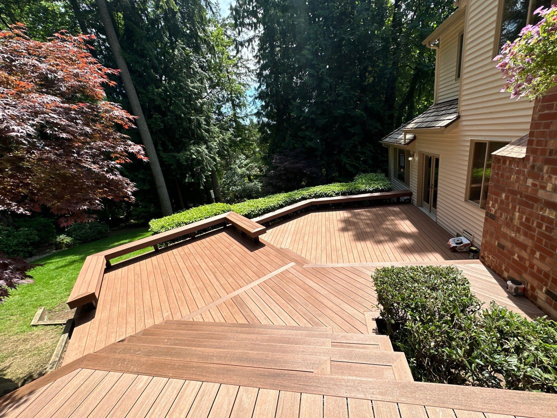 Curved composite deck with built-in benches set against a lush Pacific Northwest garden, by Ascend General Contractors