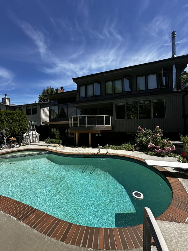 In-ground pool with brick coping next to a modern dark-stained Pacific Northwest home with new outdoor living deck